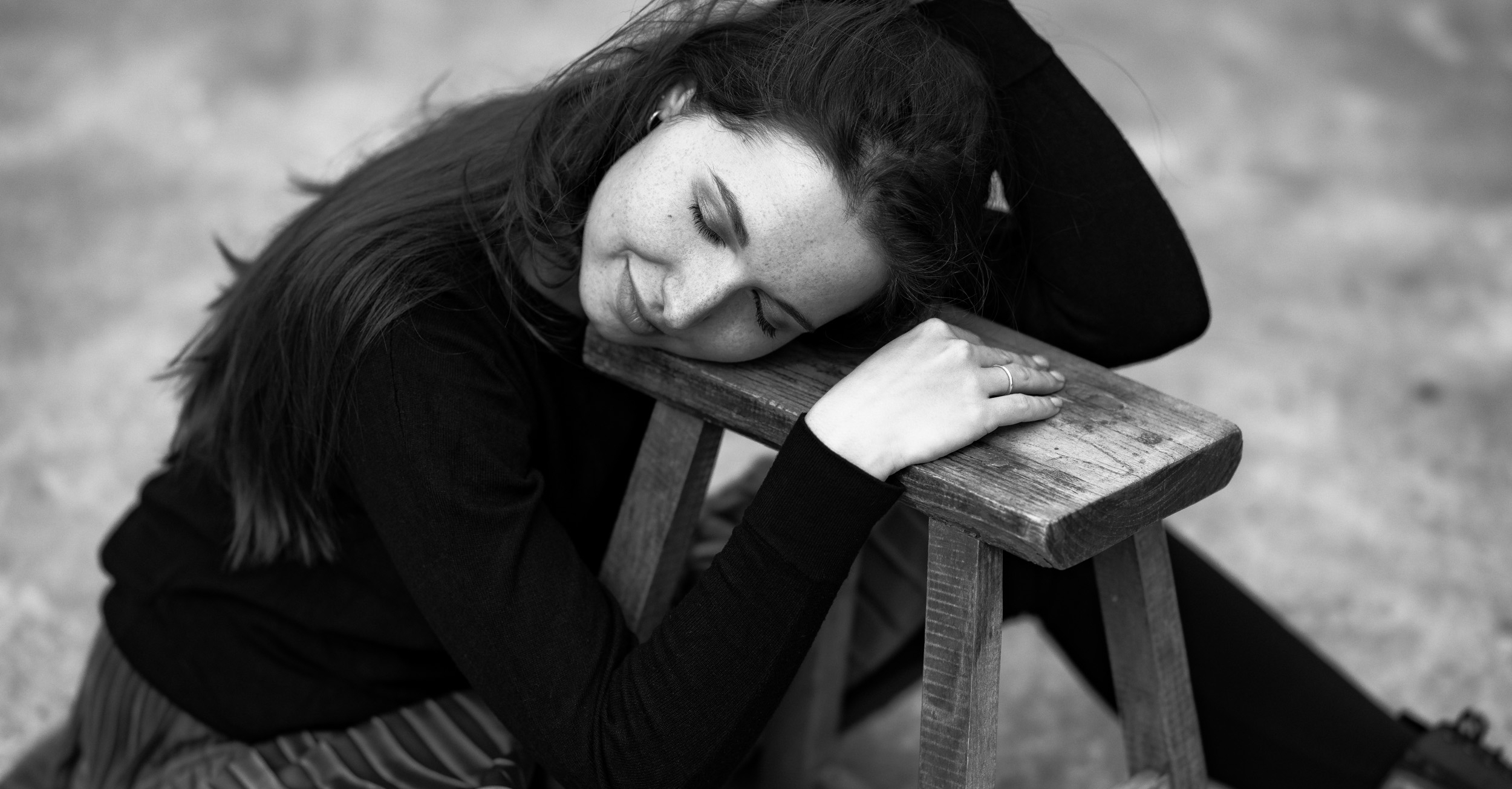 Schwarz weiß Foto von Kristin auf dem Boden sitzend den Kopf auf einen Hocker gelegt die Augen geschlossen Outdoor in Hannover.
